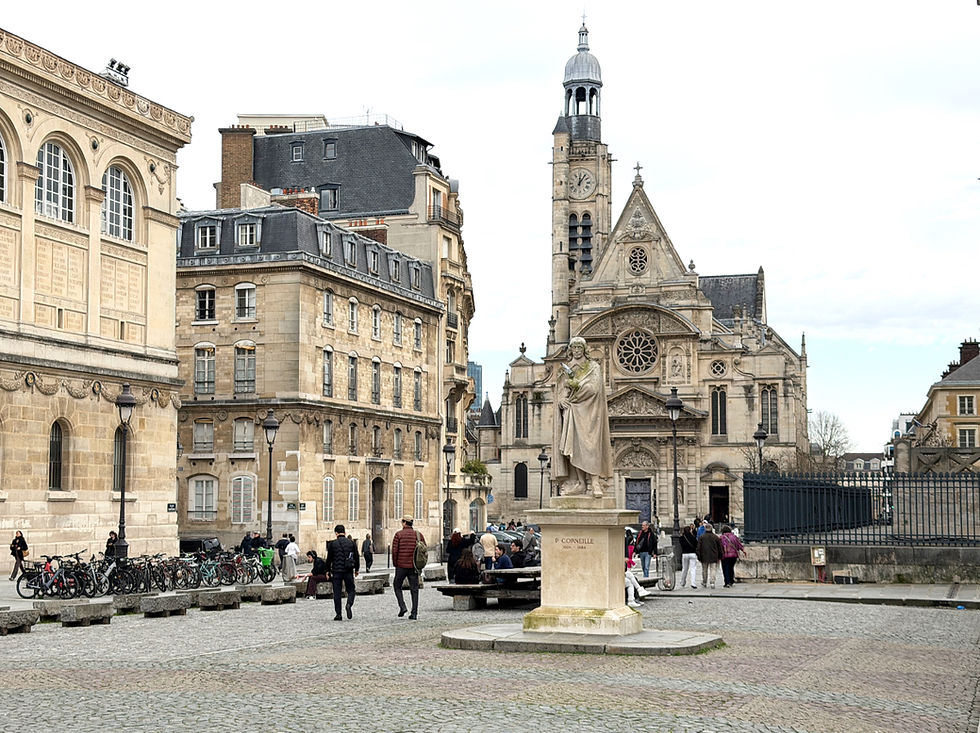 Historic square with people walking and sitting near a statue of P. Corneille. Background features ornate stone buildings and a church. Latin Quarter in Paris.