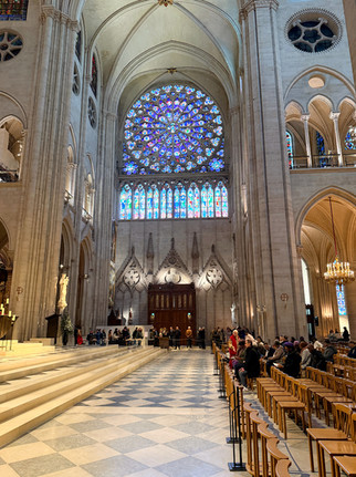 Hall way inside the Notre Dame cathedral in Paris feature rose windows and tinted glass. Patrons wait for the mass service to start as others Neal down and pray. Historic sites in Paris.