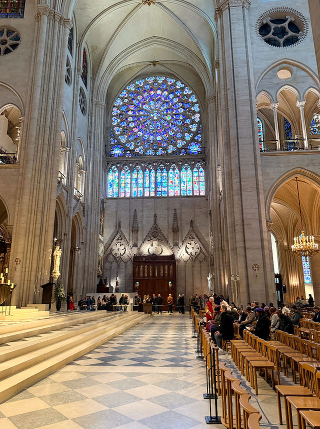 Hall way inside the Notre Dame cathedral in Paris feature rose windows and tinted glass. Patrons wait for the mass service to start as others Neal down and pray. Historic sites in Paris. 
