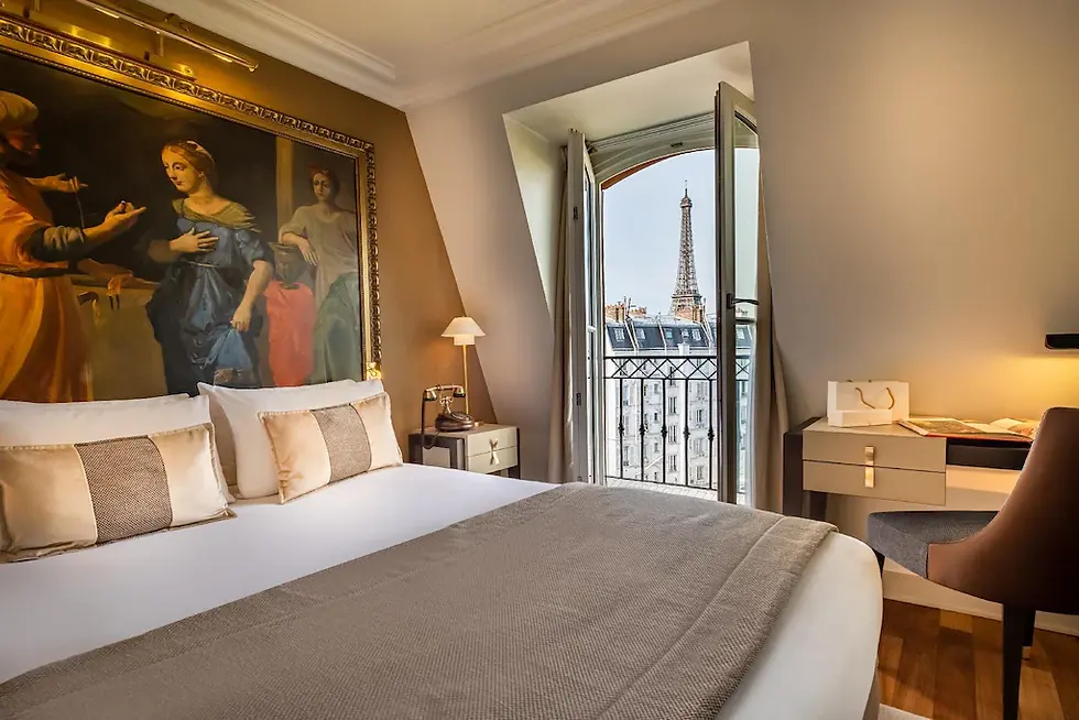 A cozy hotel room with a bed, artwork on the wall, and a view of the Eiffel Tower through open balcony doors. Warm lighting and soft colors. Where to stay in Paris for a first time visit.