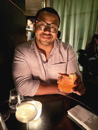 Man looks at the camera with a cocktail in hand, he wears glasses and has a smile on his face. Nightlife in Paris.