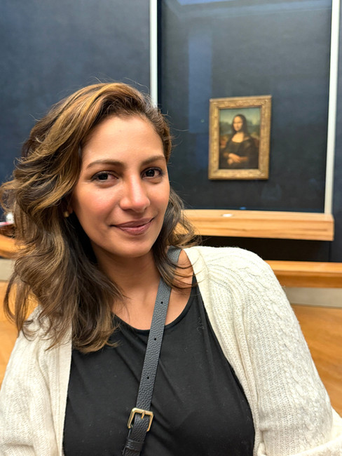 Woman standing in front of the Mona Lisa painting at the Lovre Museum.