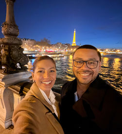 Couple standing on Pont Alexandre III in Paris with the Seine river and Eiffel Tower in the background.