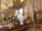 Elegant room with a marble bust on a mantel, flanked by ornate gold vases. The lavish decor includes a floral pattern and rich textures. Marie Antoinette's Chambers inside the Palace of Versailles.