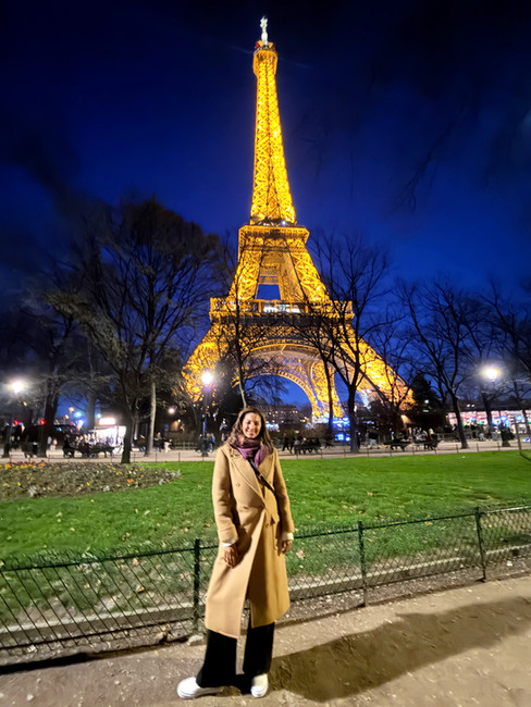 Woman in a trench tan coat posing in front of the Eiffel Tower at night in Champ de Mars