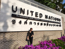 หญิงสาวยืนหน้าป้าย United Nations พร้อมข้อความและดอกไม้สีม่วงด้านหน้า