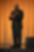Mark V Smith professional keynote speaker standing on stage in black suit with orange backdrop