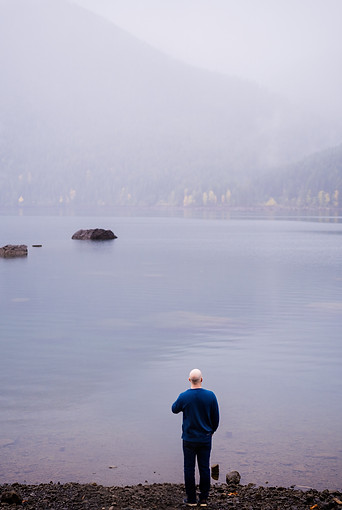 Aaron stands looking across a misty lake in the Pacific Northwest