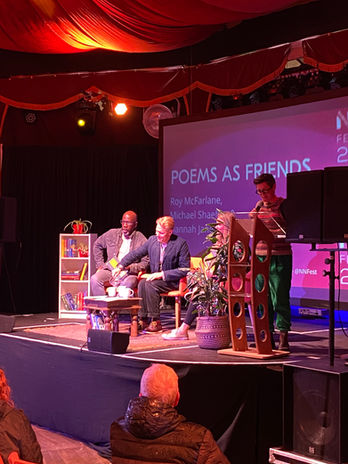 Peggy Hughes from the National Centre for Writing stands at a lectern and introduces our readers for the event: Michael Shaeffer, Roy McFarlane and Hannah Jane Walker.