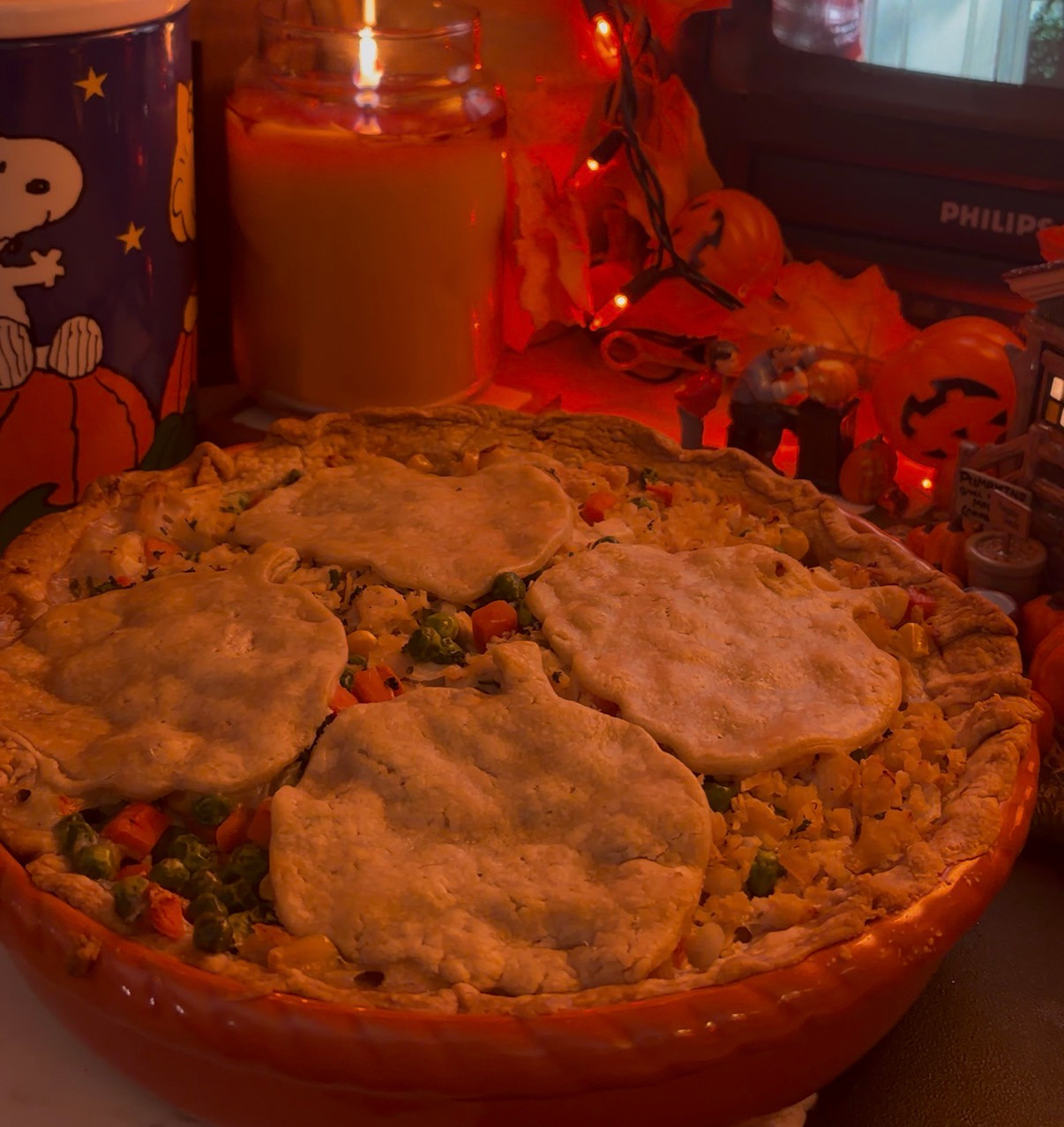 Warm autumn vibes with a comforting homemade pot pie, surrounded by festive Halloween-themed decorations, a glowing candle, and a classic movie on the TV screen.