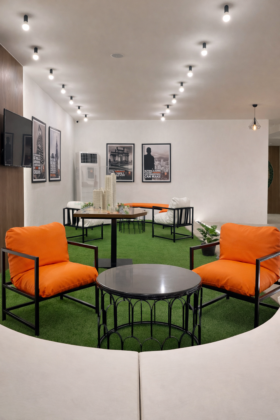 Modern sales lounge seating area with orange accent chairs and architectural model display designed by Woods & Bricks