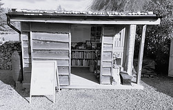 Wooden cabin with open doors, books inside and a sign, Pre-Loved Cabin