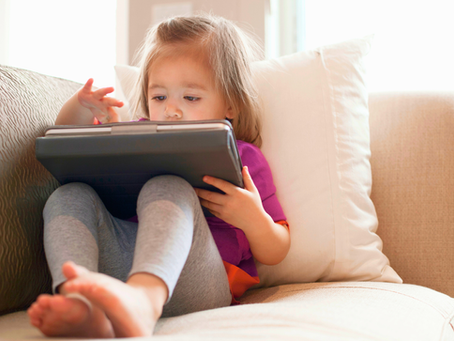 Young child sitting and watching content on an iPad, representing screen time and its impact on communication development.