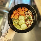 Hand holding food bowl with sweet potato, cucumber, chicken