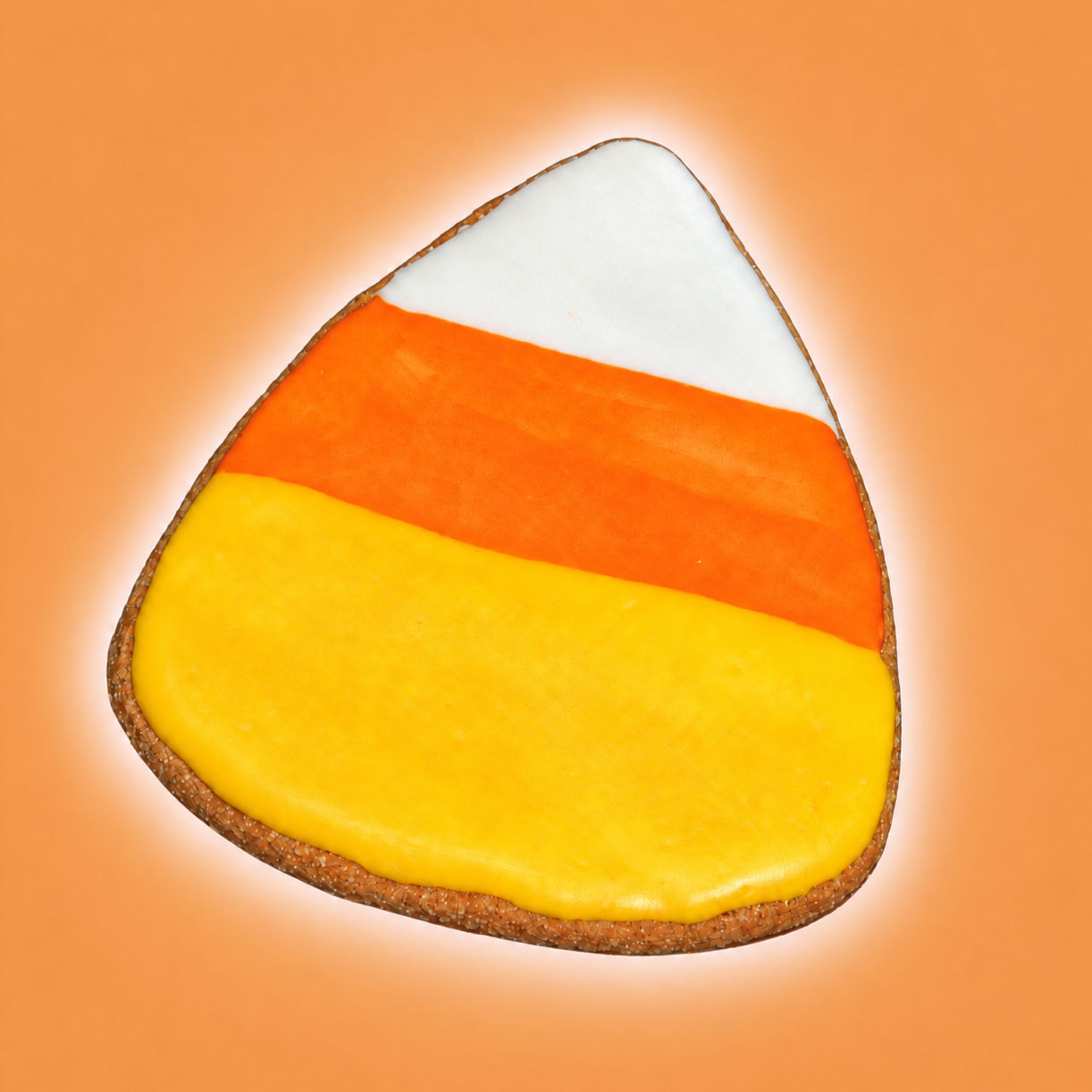 Candy corn Halloween dog cookie with yellow, orange and white icing on a warm orange background