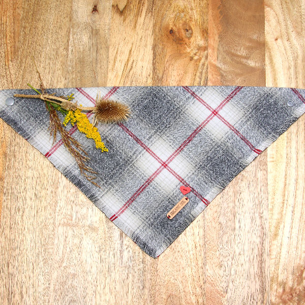 Silver Fog plaid dog bandana in gray and white with red accents, frayed edge and snap closure on wood
