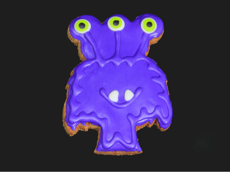 Purple three-eyed monster Halloween dog cookie with dog-safe icing on black background