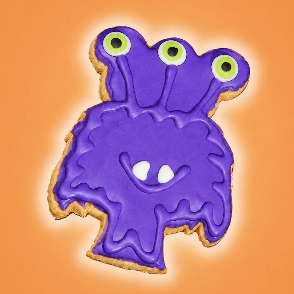 Purple three-eyed monster Halloween dog cookie with green eyes and white fangs on warm orange background