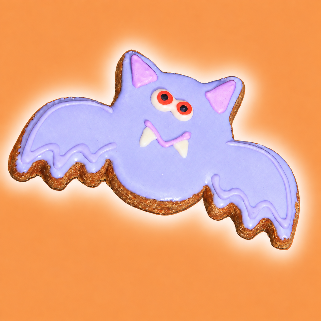 Purple bat Halloween dog cookie with lavender icing, pink ears, red eyes and white fangs on orange background