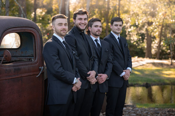Rustic outdoor portrait of the groom and his groomsmen standing together in natural scenery, showcasing candid wedding-day camaraderie.