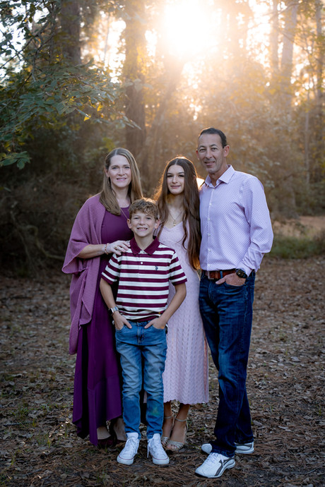 Willis, TX family photography — family of four standing together for a posed fall portrait surrounded by vibrant autumn leaves in a scenic outdoor setting. Captured by Endearing Reflections, top family and lifestyle photographer in Willis, Texas.