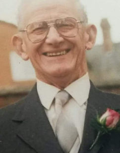 Photo of Bill, Caz's dad. He is smiling, wearing a suit, tie and glassses.