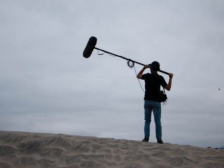 Outdoor microphone operator on a sandy dune illustrating wind-protection challenges for beach wedding ceremony audio.