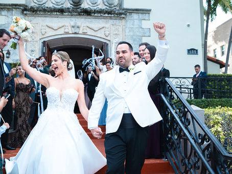 Bride and groom celebrating as they walk down the church steps, holding hands with arms raised and guests cheering around them, captured by a Miami wedding photographer