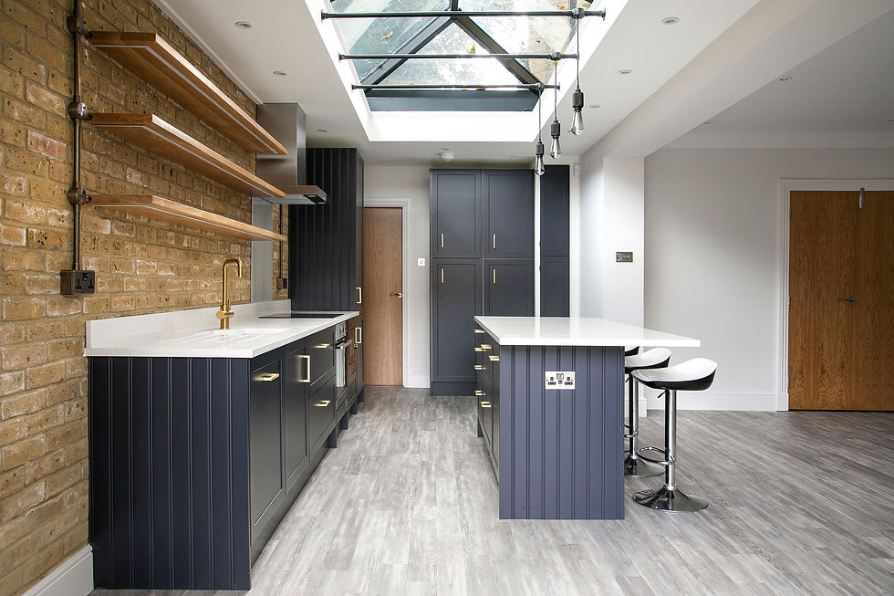 Modern kitchen with navy cabinets, white countertops, and a skylight. Brick wall with wooden shelves, bar stools, and grey flooring.