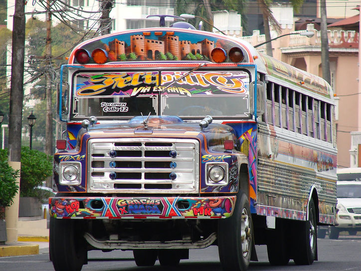 A brightly decorated, colorful truck driving through a city street, adorned with vibrant patterns and ornaments typical of Latin America transport art.