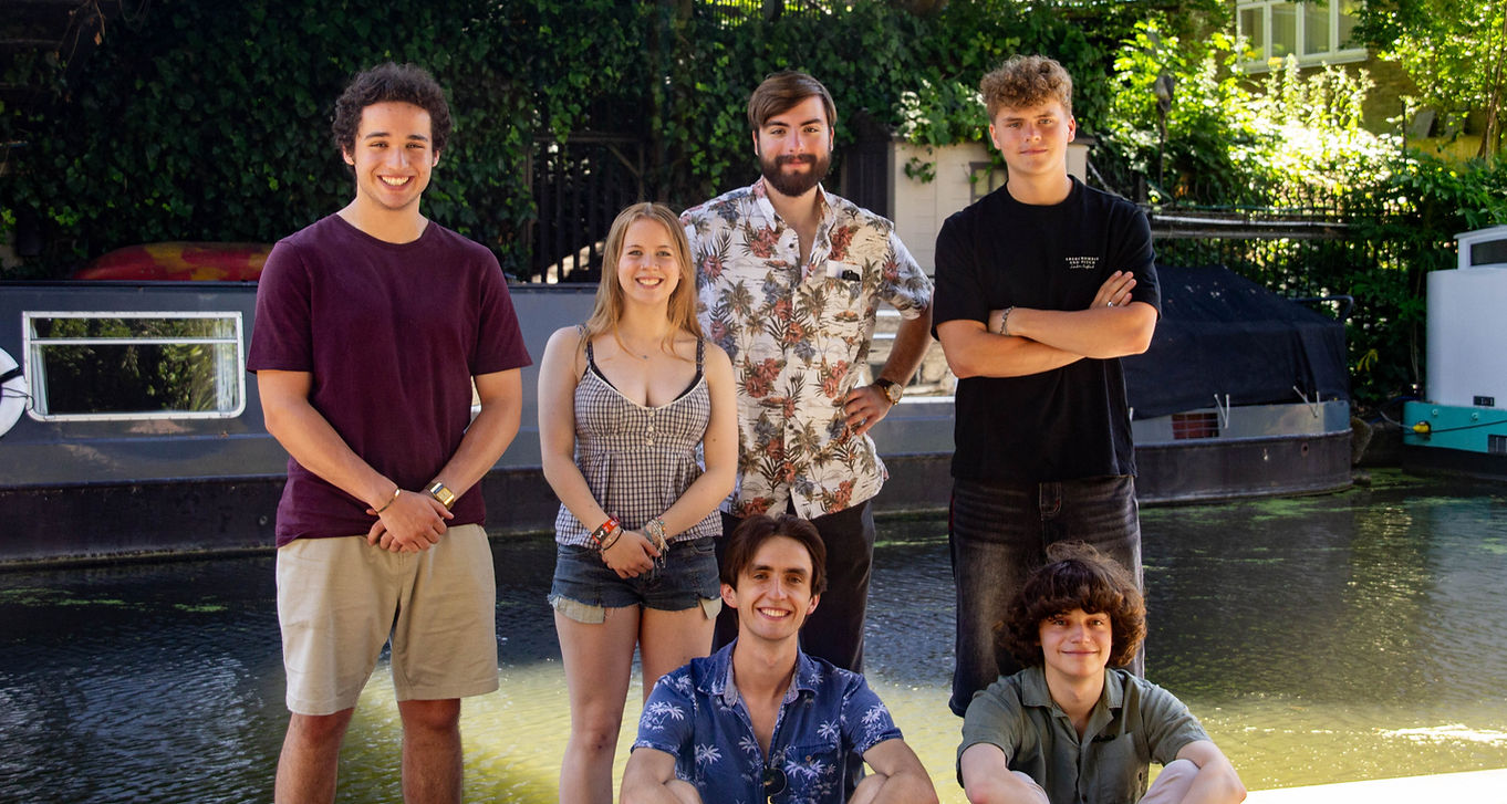 Six band members standing in front of a canal