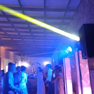 Wedding DJ playing music while people dance with professional lights and haze on dance floor.