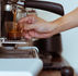 A barista holds a glass beneath an espresso machine as coffee pours into it.