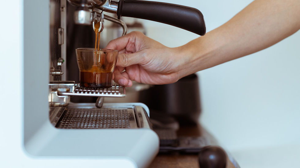 A barista holds a glass beneath an espresso machine as coffee pours into it.