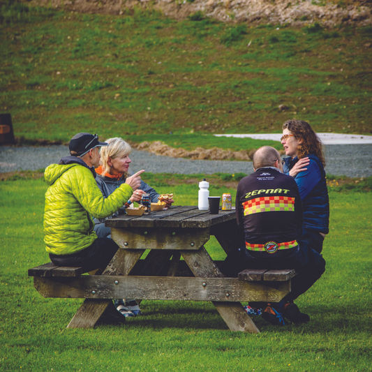 4 cyclists resting and eating at a picnic bench en route
