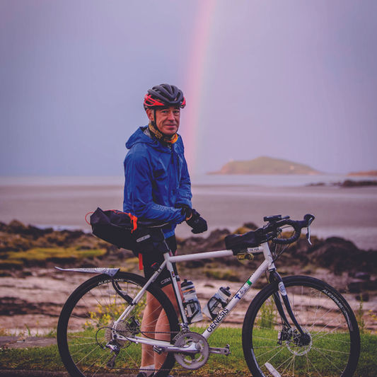 rider standing by his bike with a rainbow behind him