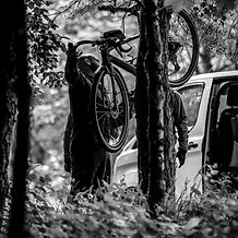 two men adjust their bike by their car