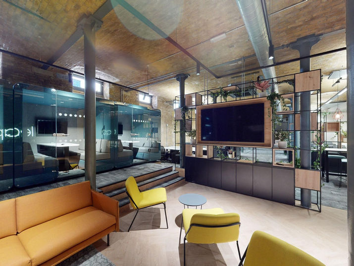 In the brightly coloured, industrial-style reception area, meeting pods sit atop a raised platform, encircled by architectural columns.