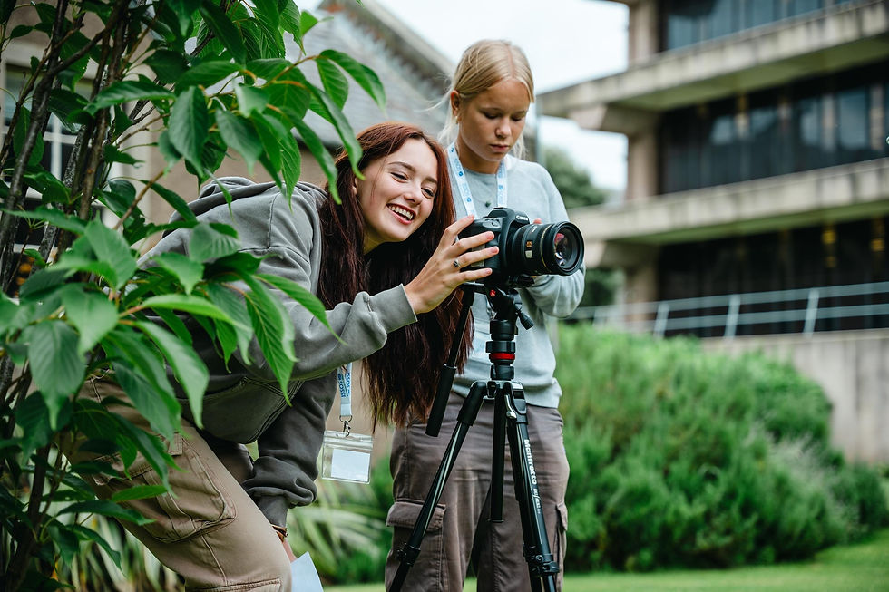 Two students working with a DSLR camera on a tripod in a garden setting, one adjusting the camera while the other looks on.