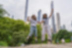 Two students jumping and smiling in Central Park, New York City, with skyscrapers in the background.