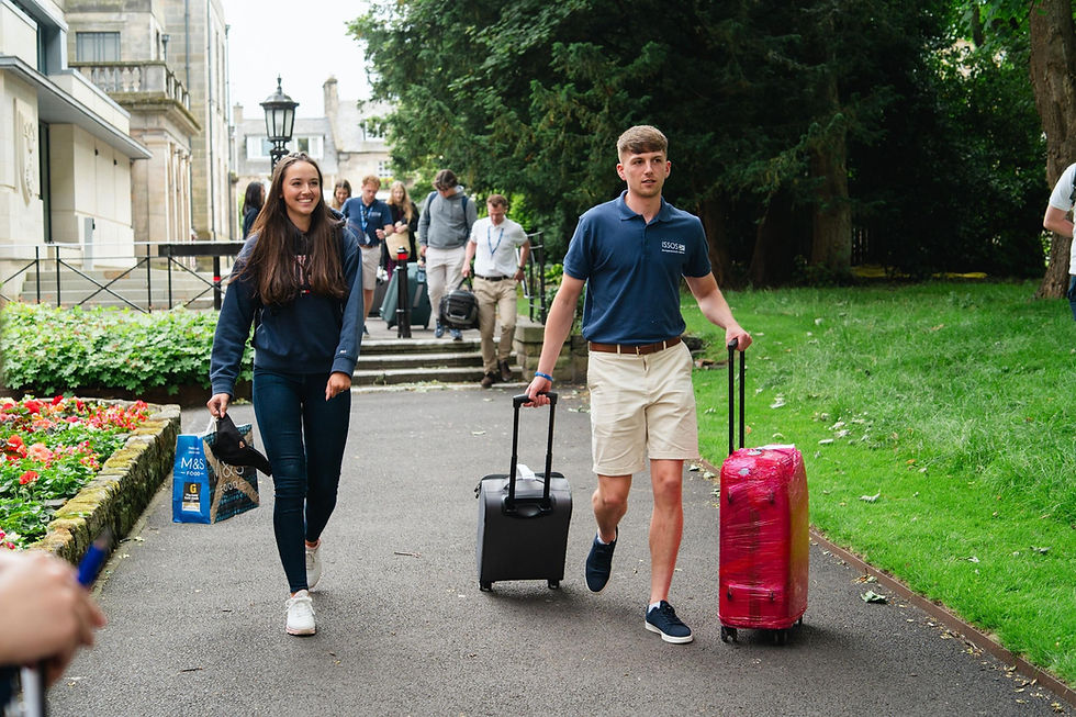 Student arriving at ISSOS campus with counselor carrying suitcases and walking up a path.