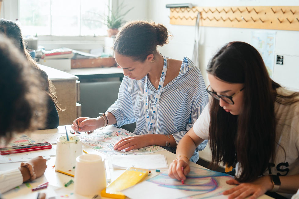 Students focused on creating colourful drawings during an art lesson, seated around a table with pencils and pastels.