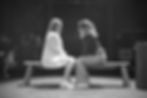 Two actors facing each other sat on a bench during rehursals for Star Cross'd.