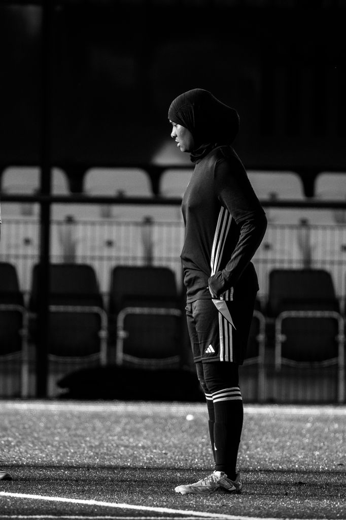 A black and white portrait of a woman coach standing on a football pitch