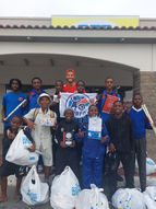 Tony steht lächelnd zwischen einer Gruppe namibischer Schulkinder, die bunte neue Schulrucksäcke tragen und Daumen nach oben zeigen.