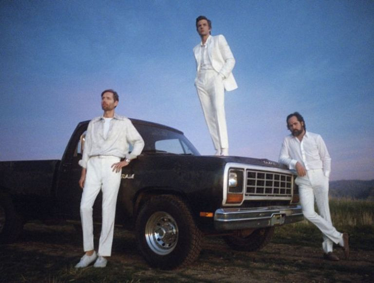 The Killers dressed in all white, posing with a black truck