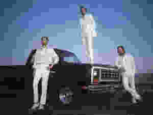 The Killers dressed in all white, posing with a black truck