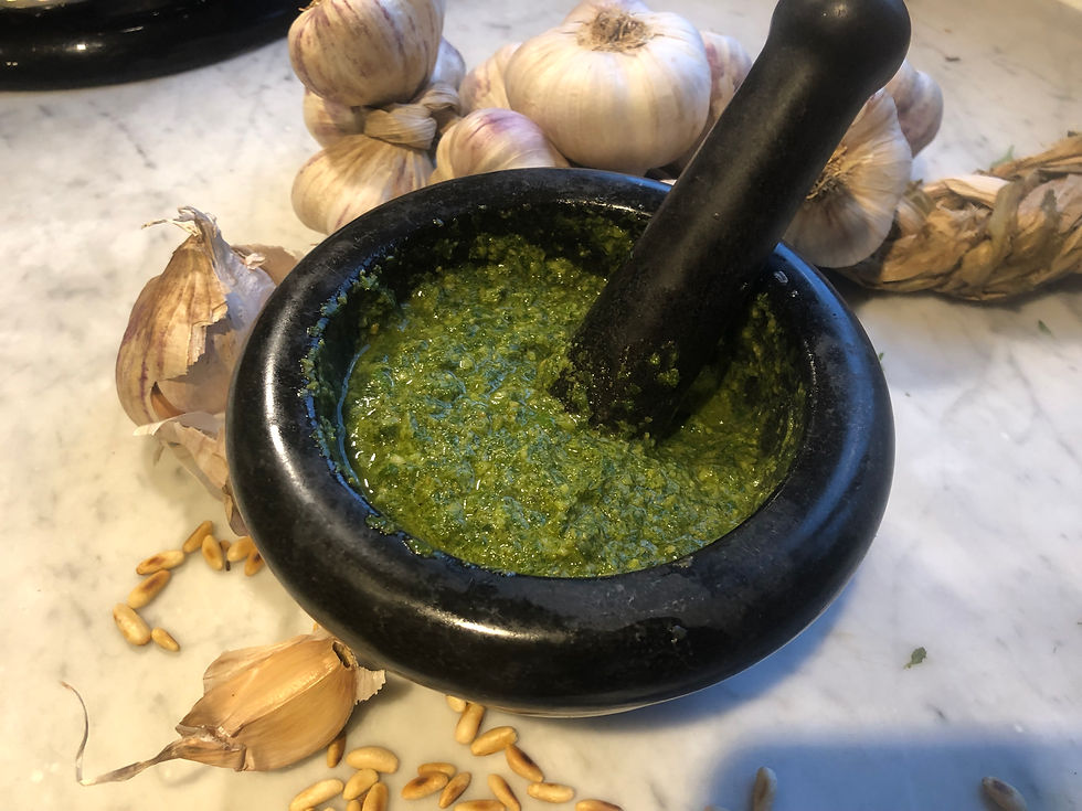 Basilikum Pesto in einem Mörser. Auf der Marmorarbeitsfläche liegen Knoblauchzehen