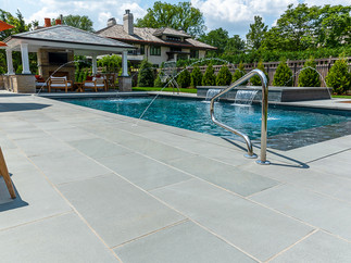 Swimming pool deck with view of cabana and pergola outdoor kitchen in background.