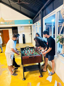 Group of backpackers playing foosball in a vibrant hostel lounge with relaxed seating and colorful décor.